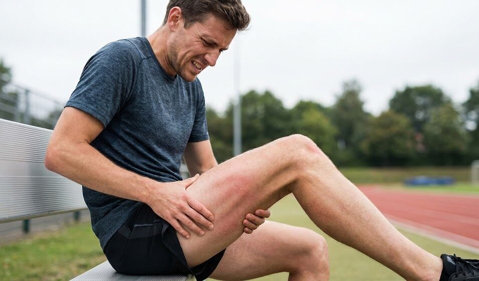 Profesjonalne ujęcie biegacza masującego obolałe udo po treningu.