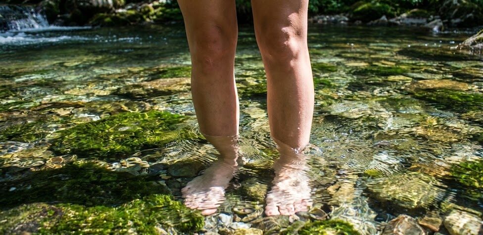 Zbliżenie na nogi zanurzone w krystalicznie czystym, zimnym górskim strumieniu