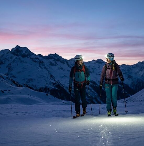 Zdjęcie pary narciarzy skiturowych idących ramię w ramię o zmierzchu.
