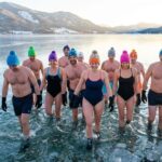 Zdjęcie przedstawiające grupę uśmiechniętych osób w kolorowych czapkach i rękawiczkach, wychodzących zdecydowanym krokiem do krystalicznie czystego