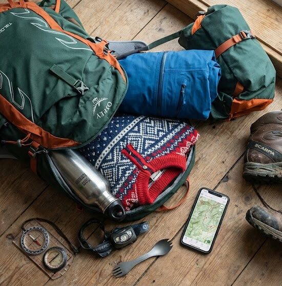 Kadr pokazujący otwarty, nowoczesny plecak turystyczny leżący na drewnianej podłodze.