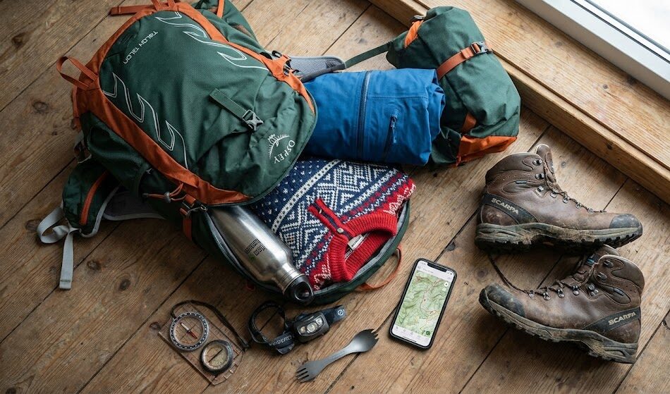 Kadr pokazujący otwarty, nowoczesny plecak turystyczny leżący na drewnianej podłodze.