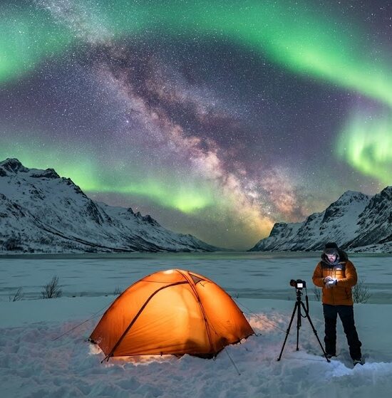 Zdjęcie realistyczne przedstawiające ośnieżony krajobraz norweski w nocy, z wyraźnym pasem Drogi Mlecznej i intensywną, zielono fioletową zorzą polarną.