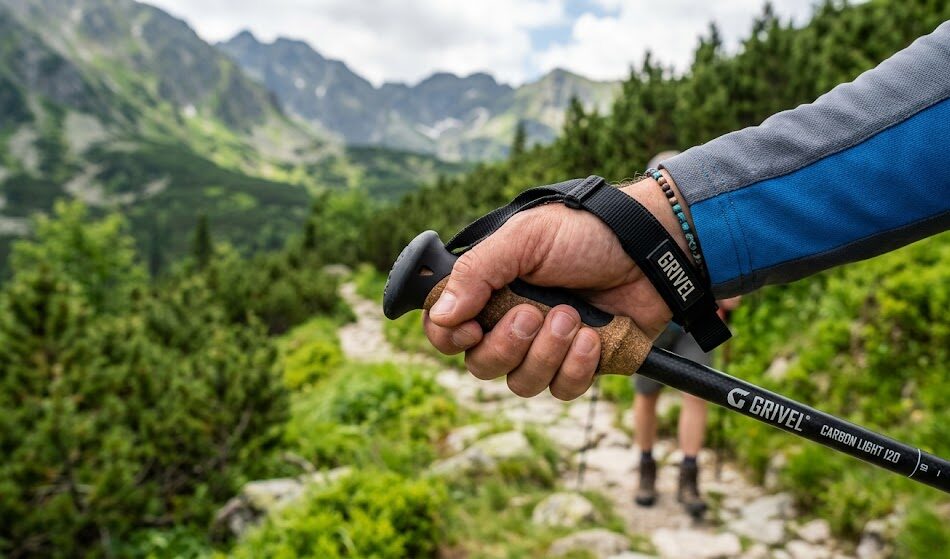 Zbliżenie na dłoń turysty trzymającego rękojeść kijka trekkingowego.